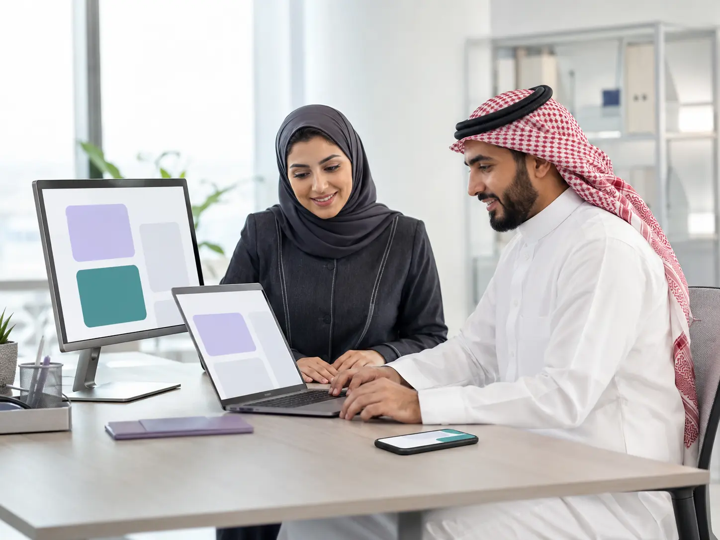 Saudi business professionals working with a laptop, desktop monitor, and smartphone